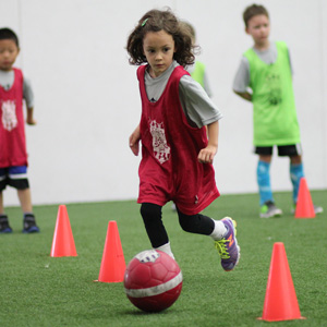 young girl dribbling soccer ball through cones