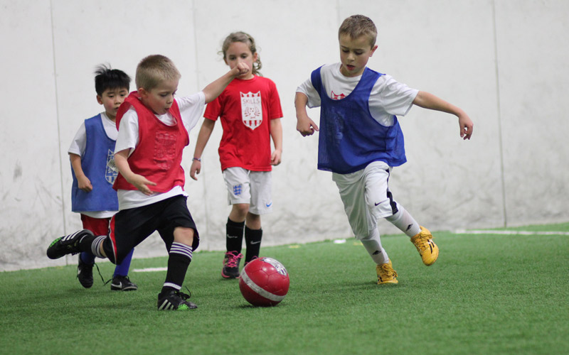 Kids kicking a red soccer ball at Skills institute classes