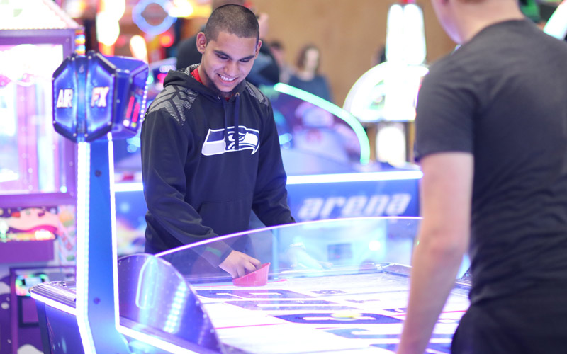 A young man smiles while playing arcade game at Arena Sports Mill Creek