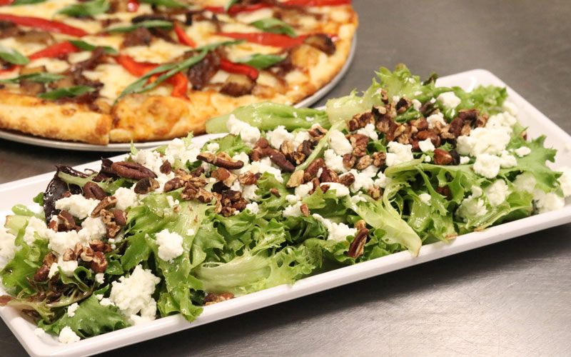 Moe's Kitchen maple salad with pizza in the background