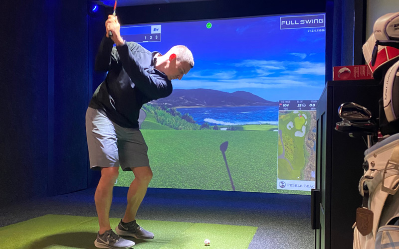 A man takes a swing while playing golf in the Sports Simulator at Arena Sports