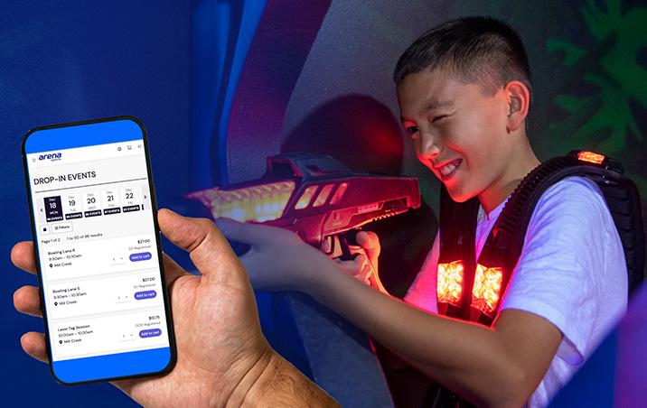 A boy plays laser tag while an adult looks at a mobile phone screen showing online reservations at Arena Sports