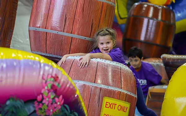 A young girl bounces through obstacles in the Inflatable Funzone during summer camp at Arena Sports