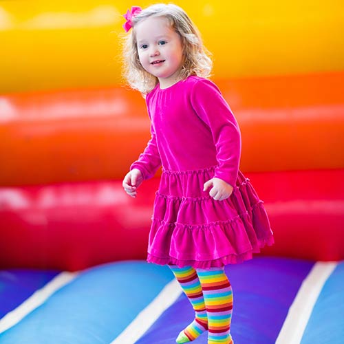 A little girl in colorful dress stands in a bouncy house