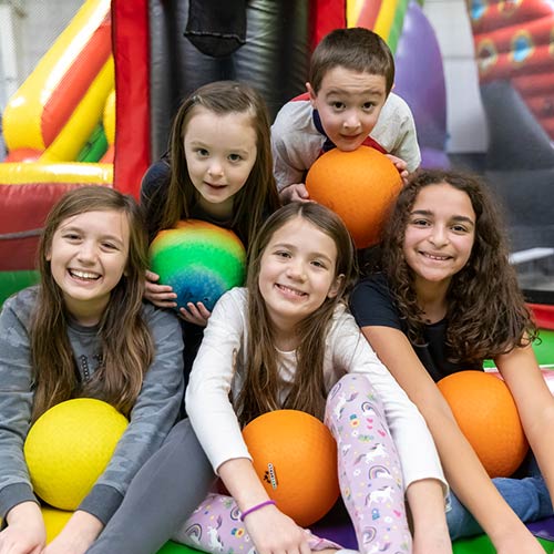 A group of kids smile while holding rubber balls in the Inflatable FunZone