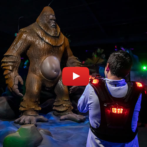An image of a man aims his laser tag gun at a statue of Sasquatch at Arena Sports in Issaquah with a Youtube icon