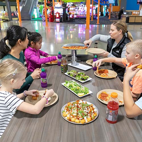 Two families enjoy pizza and drinks in the restaurant after having fun on the Ropes Course at Arena Sports Mill Creek