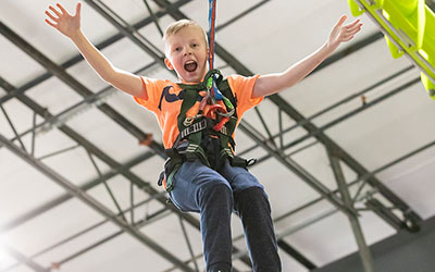 A boy wears a harness to dangle above the ground in the Ropes Course at Arena Sports Mill Creek during a group event