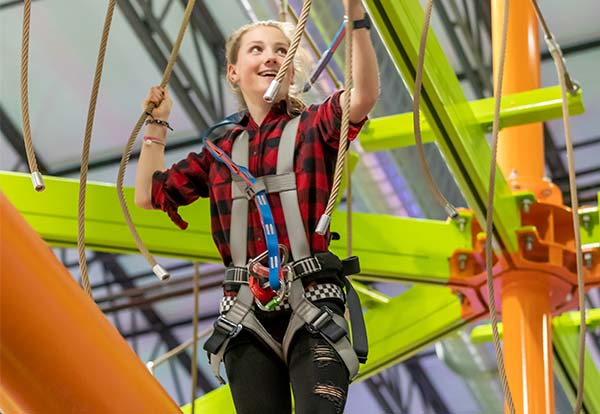 A teenager wears a harness while walking the ropes course at Arena Sports Mill Creek