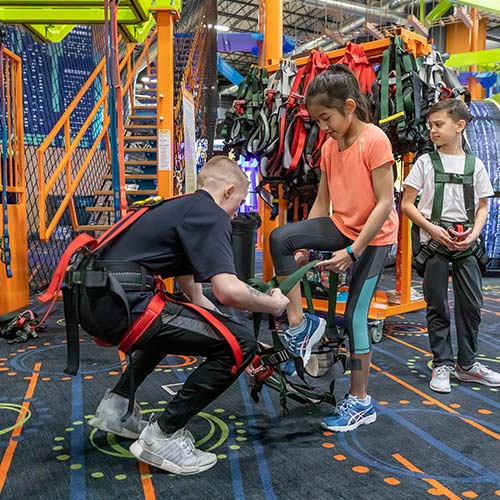 A child is helped into a safety harness before trying the Ropes Course at Arena Sports Mill Creek