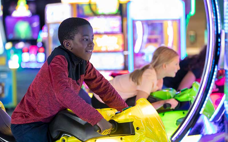 Two kids ride arcade games in the Family Entertainment Center at Arena Sports Mill Creek
