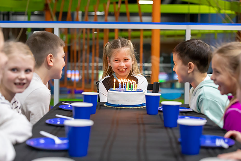 A little girl prepares to blow out candles on her cake with birthday kids surrounding her at her birthday party at Arena Sports