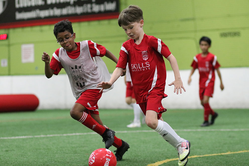 Boys in soccer uniforms play soccer during a Skills Institute class at Arena Sports