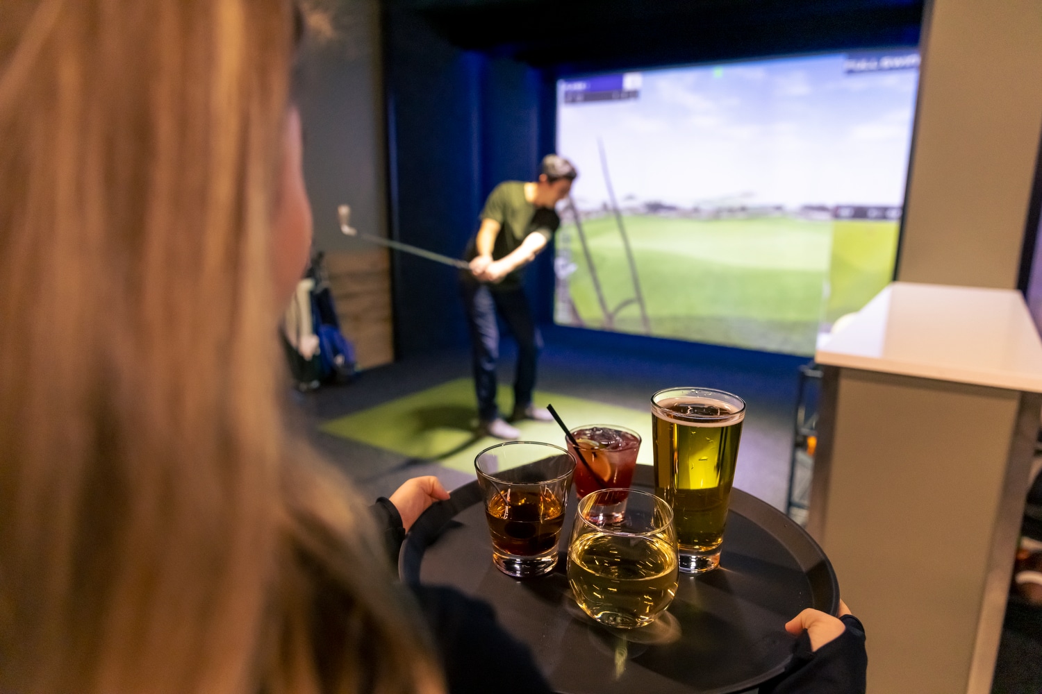 man in golf simulator, drinks being delivered