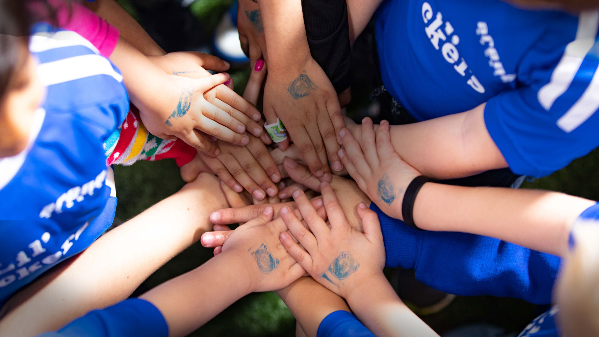 Kids hands in a circle while wearing Lil' Kickers jerseys