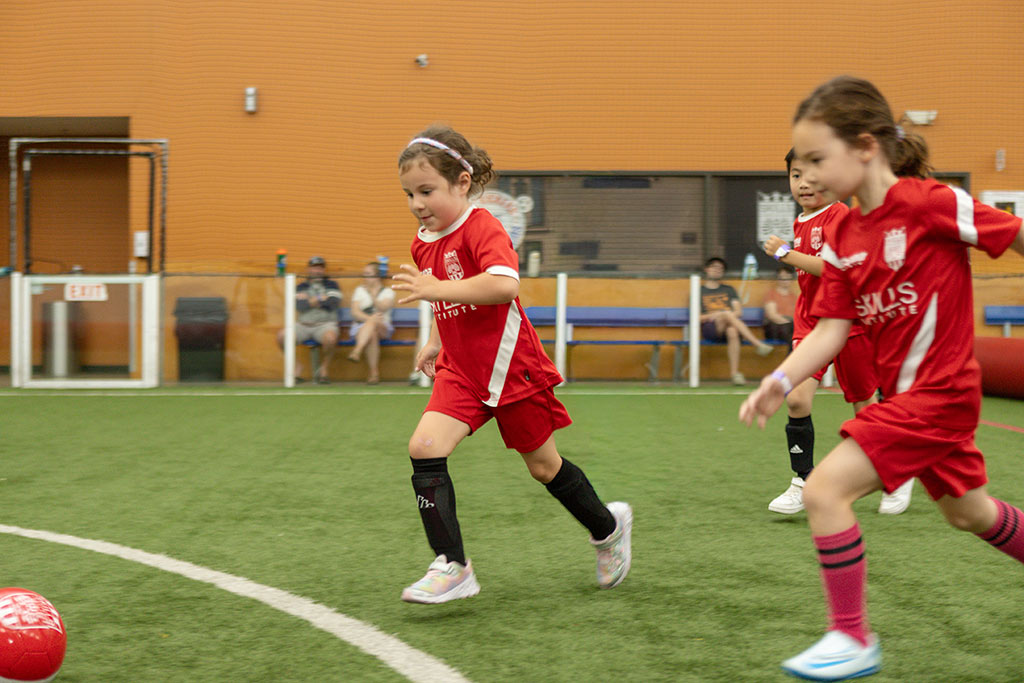Several young girls soccer league players chase the ball at Arena Sports