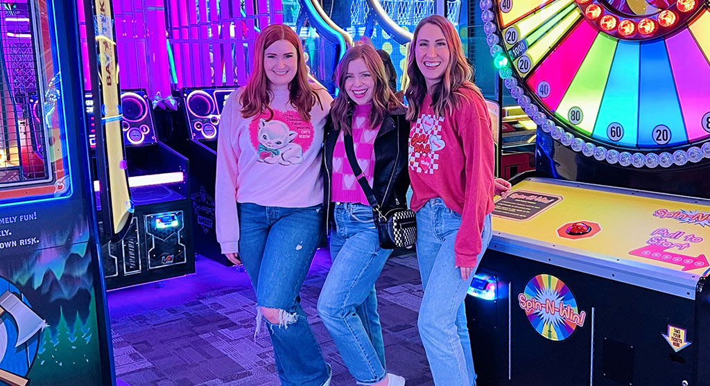 Three women pose for a picture in the arcade at Arena Sports
