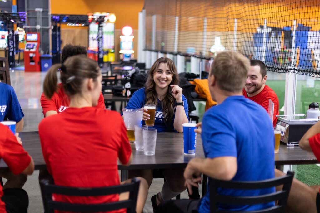 people wearing different colored soccer jersies enjoying each other's company at a table with drinks