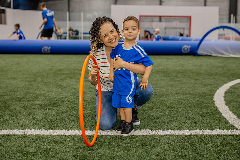 Young boy and mom smiling at camera during Lil' Kickers soccer class.