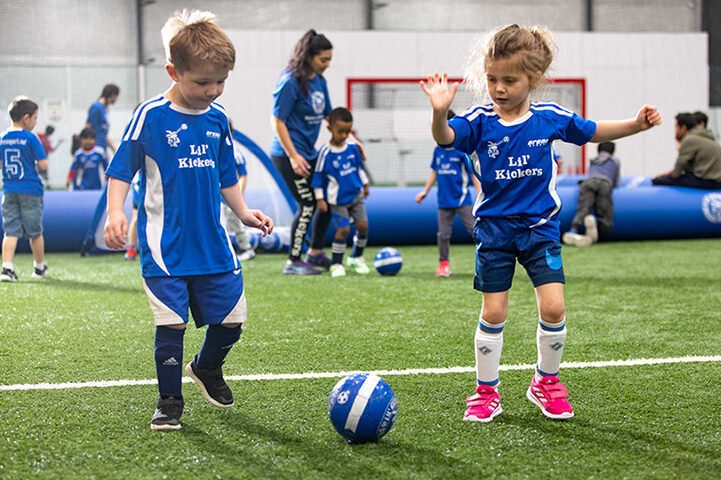 Young boy and girl playing during Lil' Kickers soccer class.
